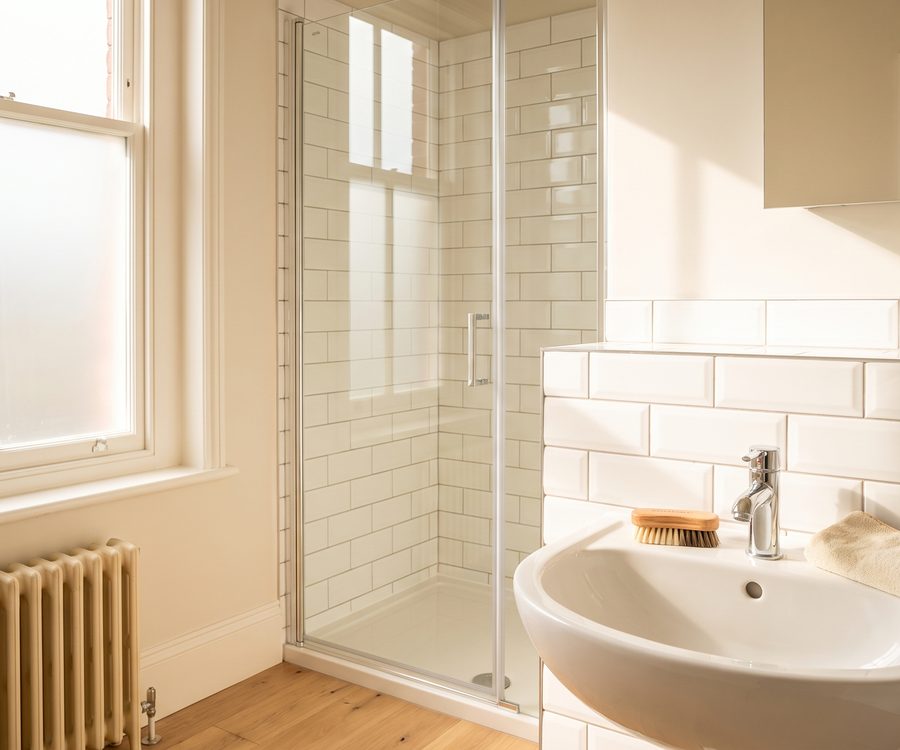 White metro tiles and a glass shower screen in a bathroom, with a detail brush and cloth on the tiled edge