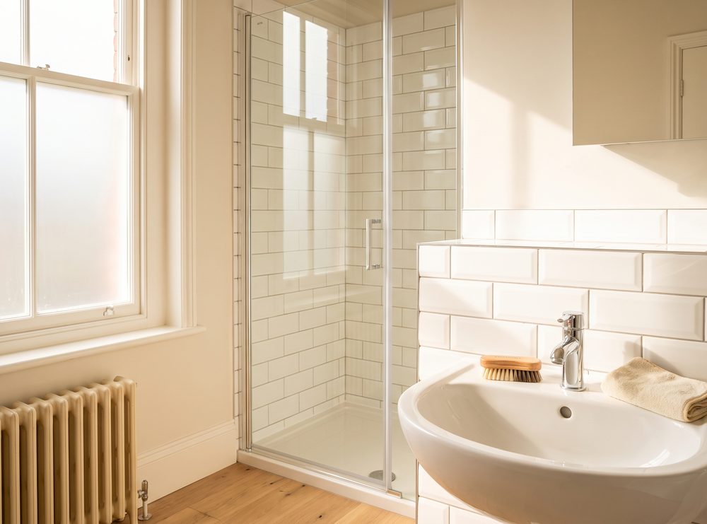 White metro tiles and a glass shower screen with a detail brush and a microfibre cloth resting on the tiled edge