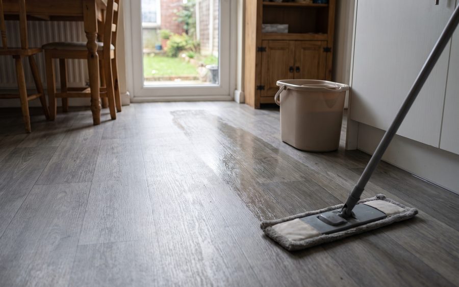 A flat head mop on grey vinyl plank flooring with a damp cleaned band across it