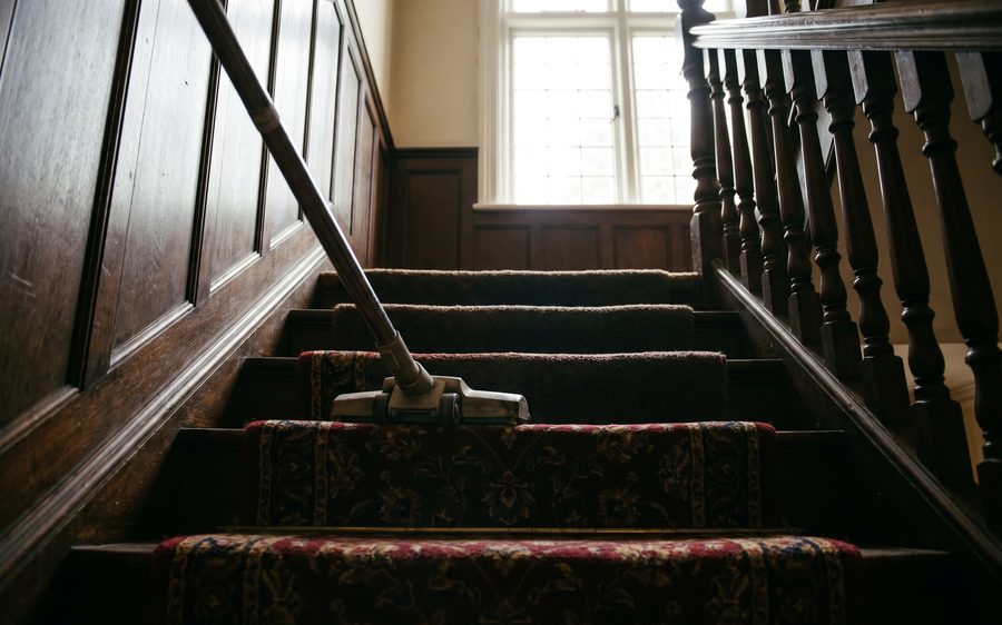 A vacuum head on a patterned stair runner in a Victorian hallway, freshly groomed pile behind it